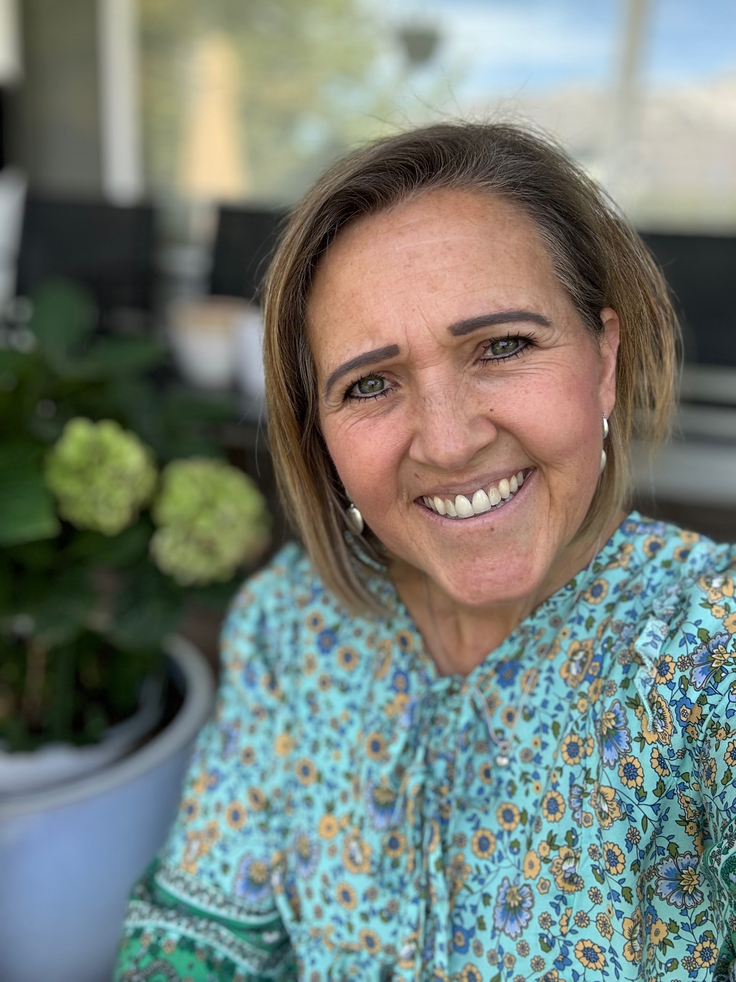 Wendy Castleton smiling outdoors in a blue and green floral blouse beside a hydrangea