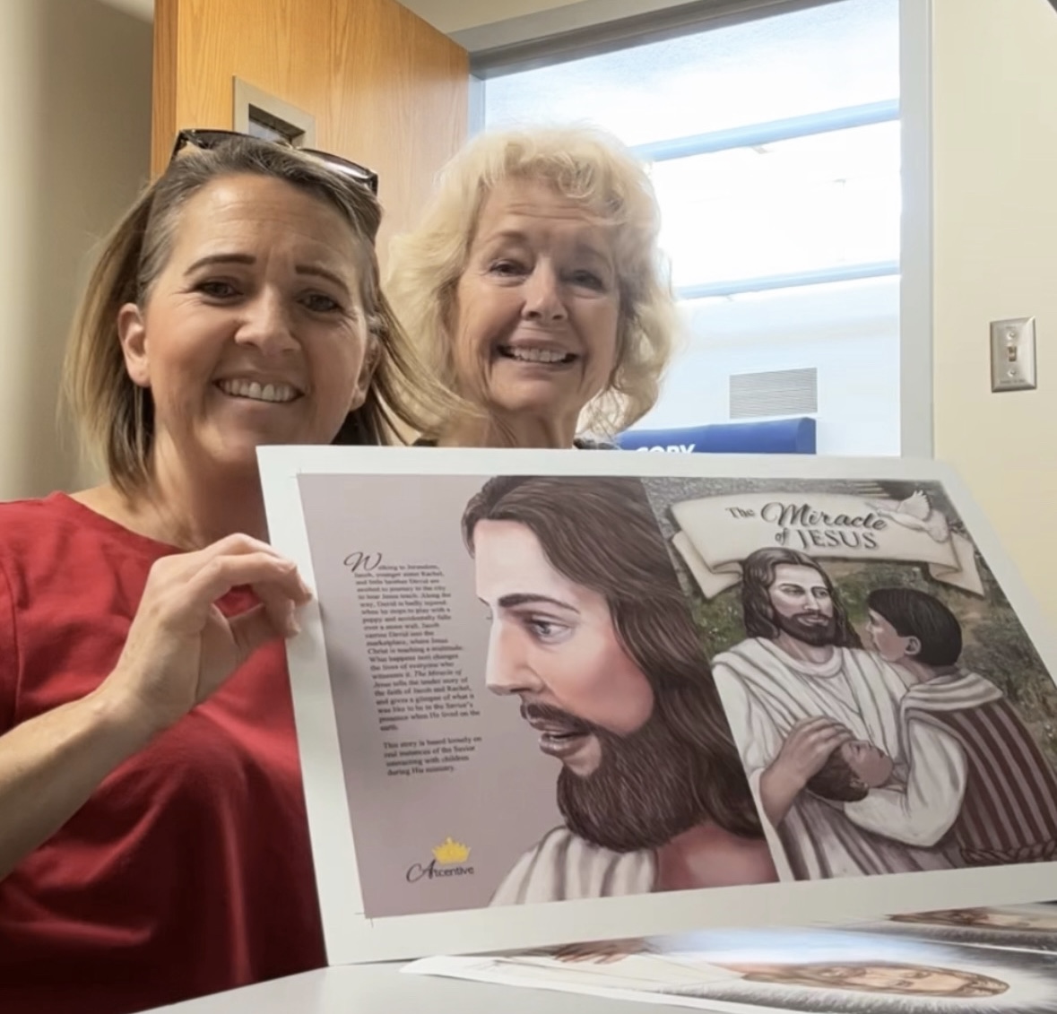 Camille Cornaby and Wendy Castleton holding a printed copy of The Miracle of Jesus