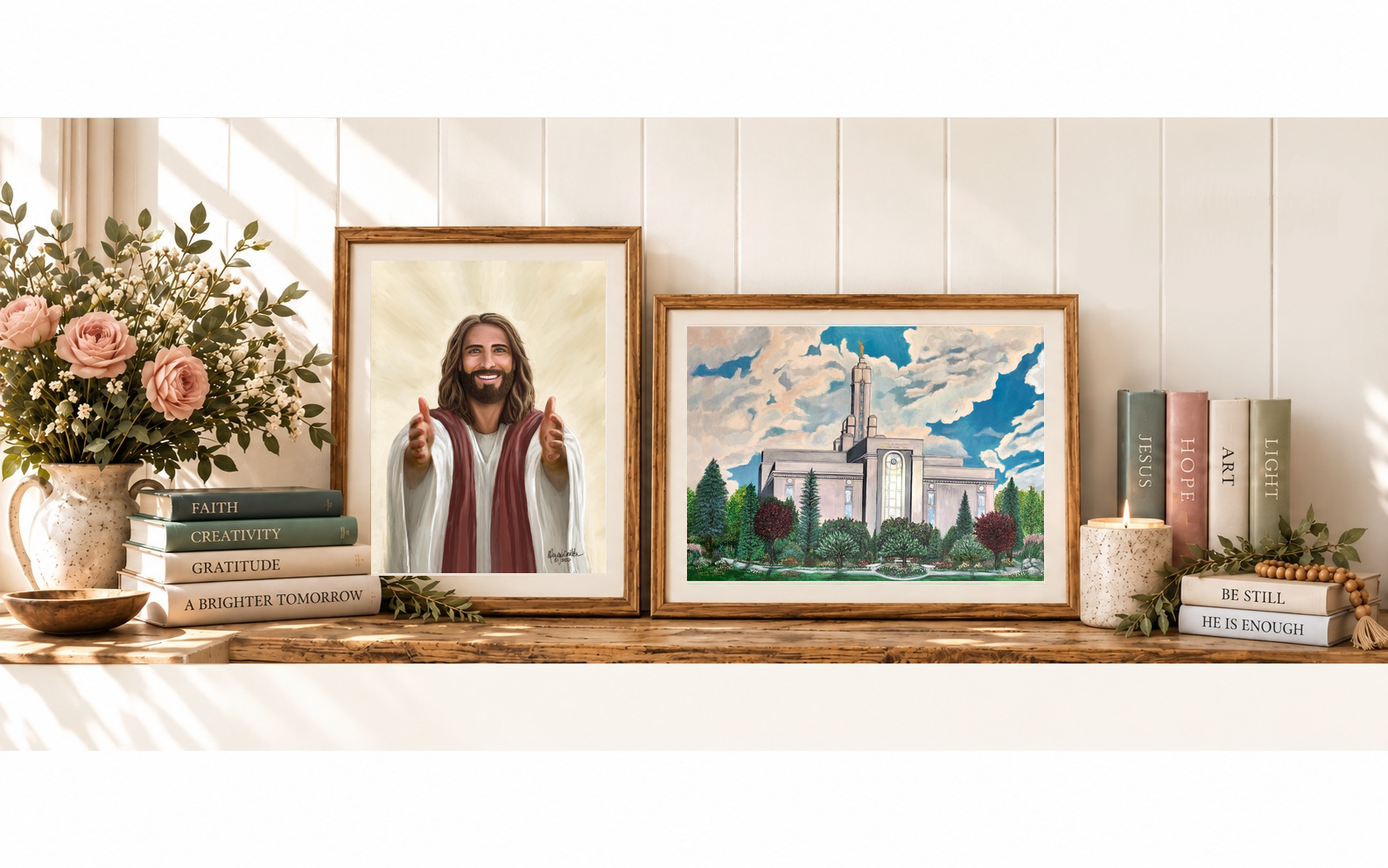 Two framed Heart Identity paintings on a wooden console: the Mt Timpanogos Temple and Jesus Christ reaching with open arms, beside books and a vase of white flowers